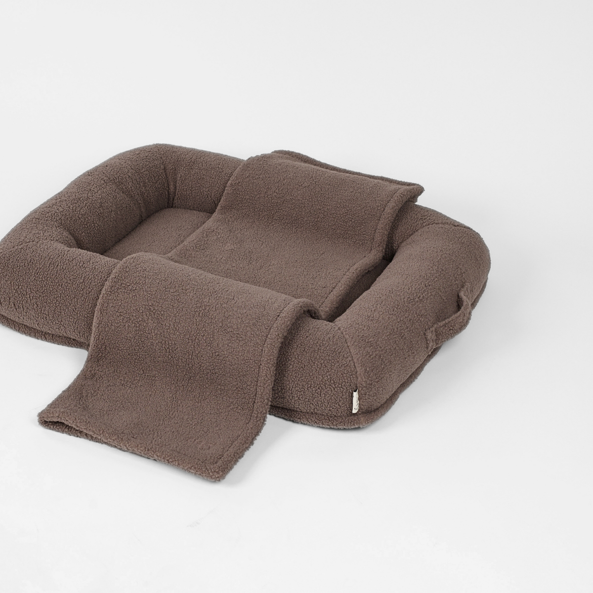 Taupe-värinen teddy-koiranpeti, jonka reunan yli on asetettu yhteensopiva peitto