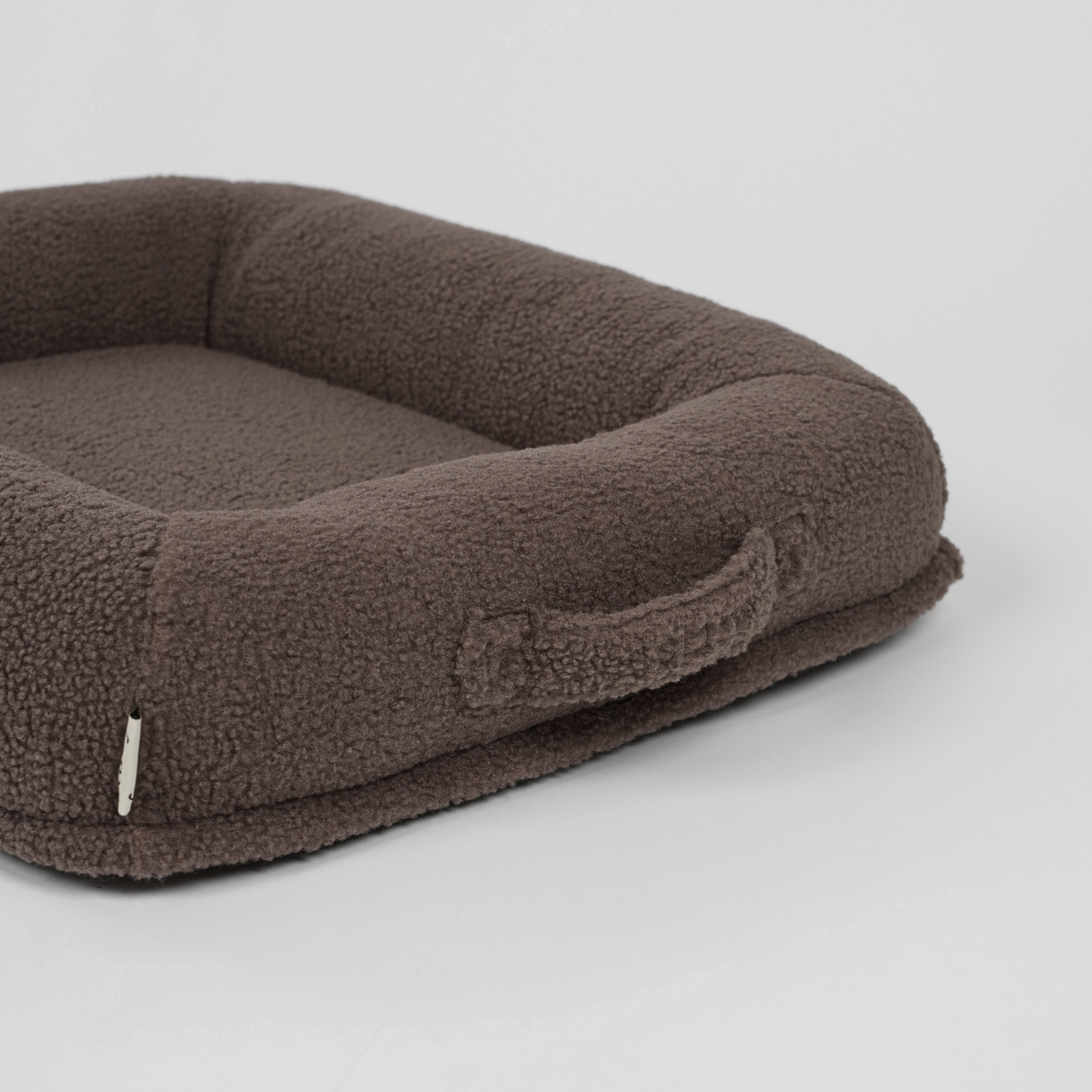 Taupe-värinen teddy-koiranpeti, kuvattu sivulta, kantokahva näkyvissä