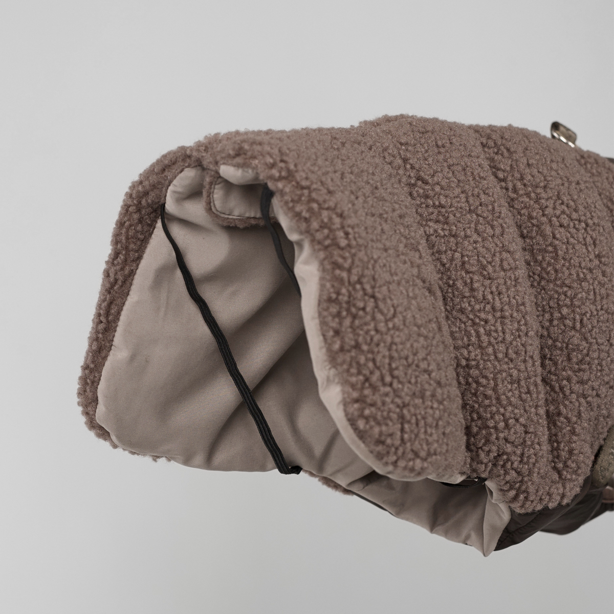 The taupe teddy dog coat rolled up, showing its lining